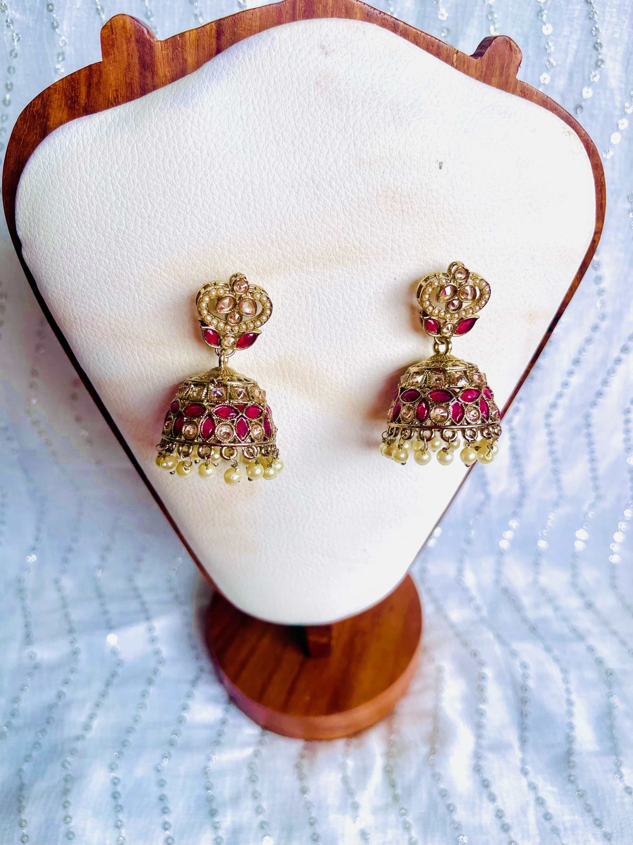 Rani Pink Taj Jhumkas dome-shaped pink and gold traditional earrings with intricate detailing and pearl accents displayed on a wooden stand
