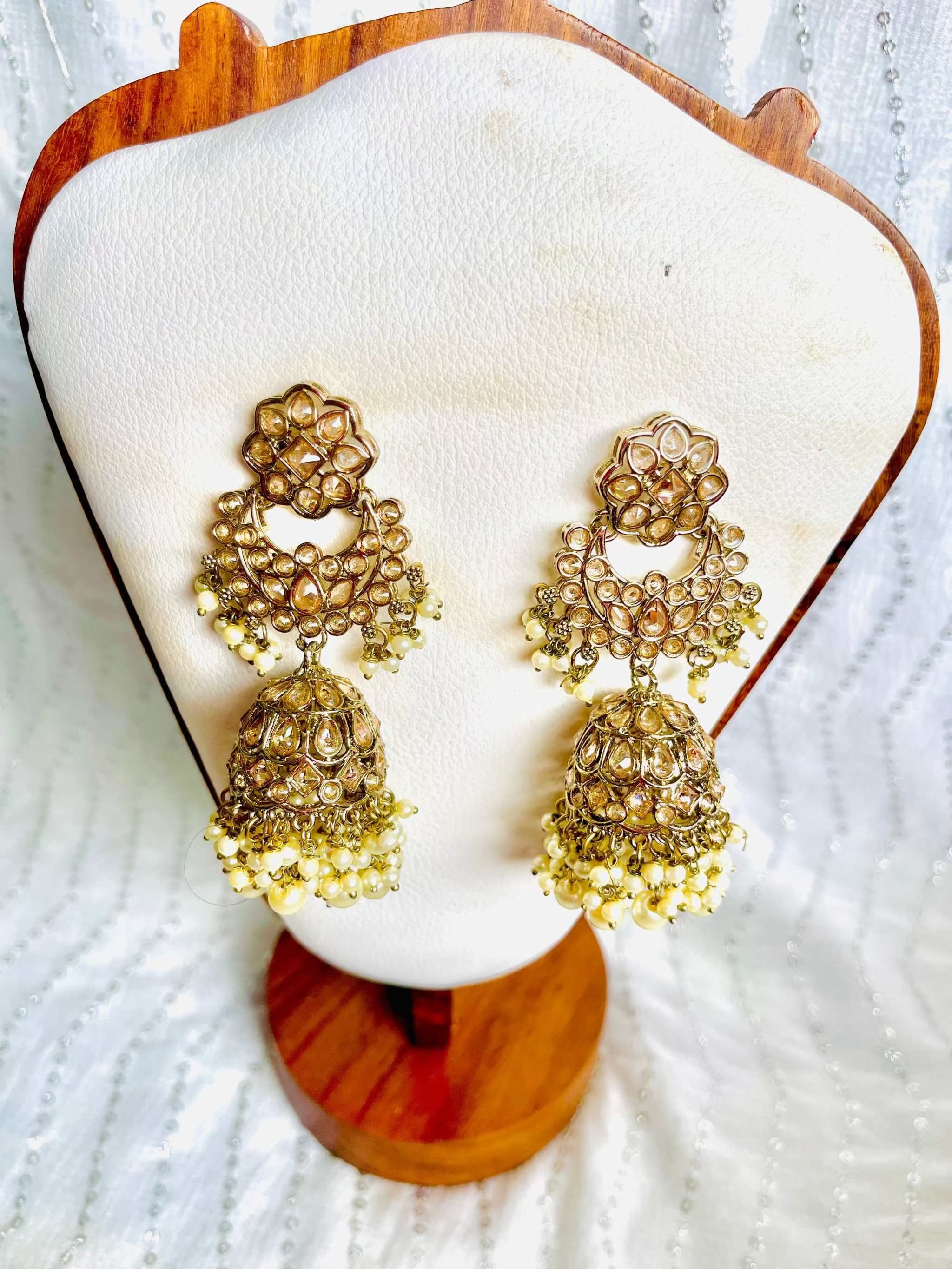 Cascading long jhumkas with tiered gold design and pearl accents displayed on a white stand