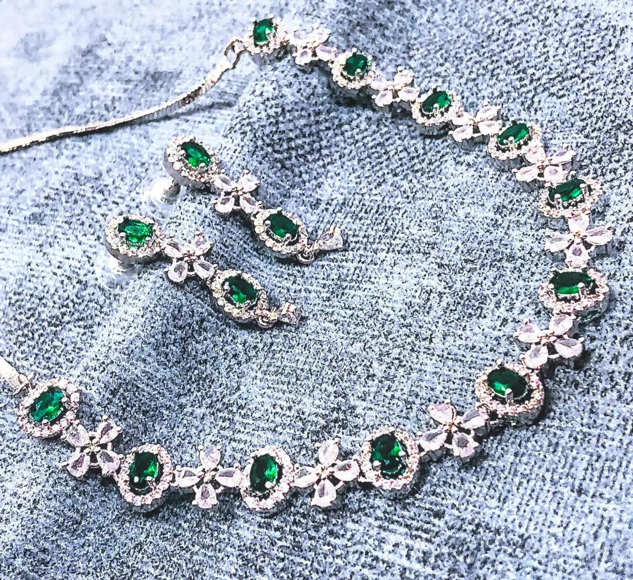 Elegant green gemstone necklace and matching earrings set with silver floral accents on a textured blue background