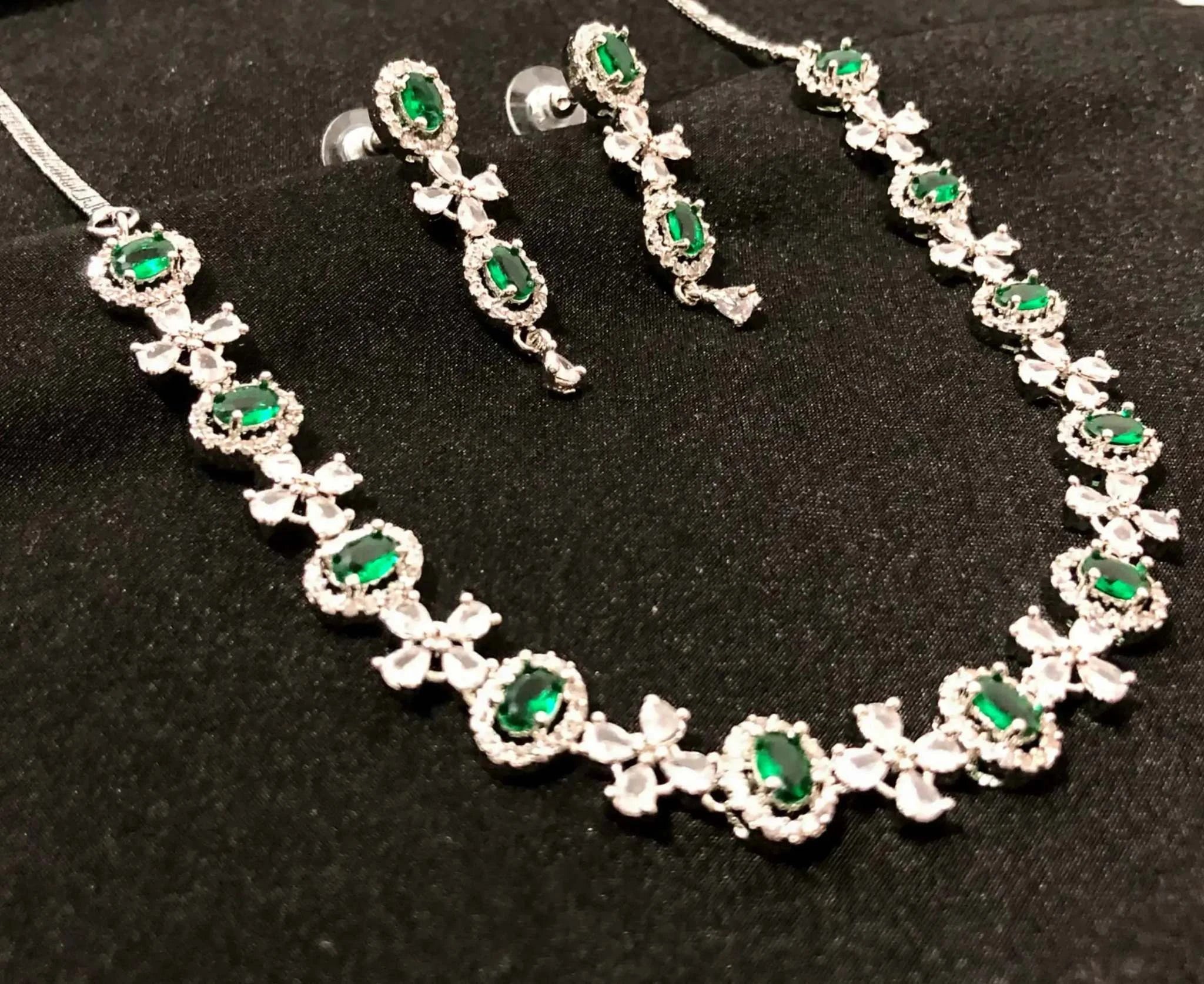 Elegant green gemstone necklace and matching earrings set with silver accents on black background