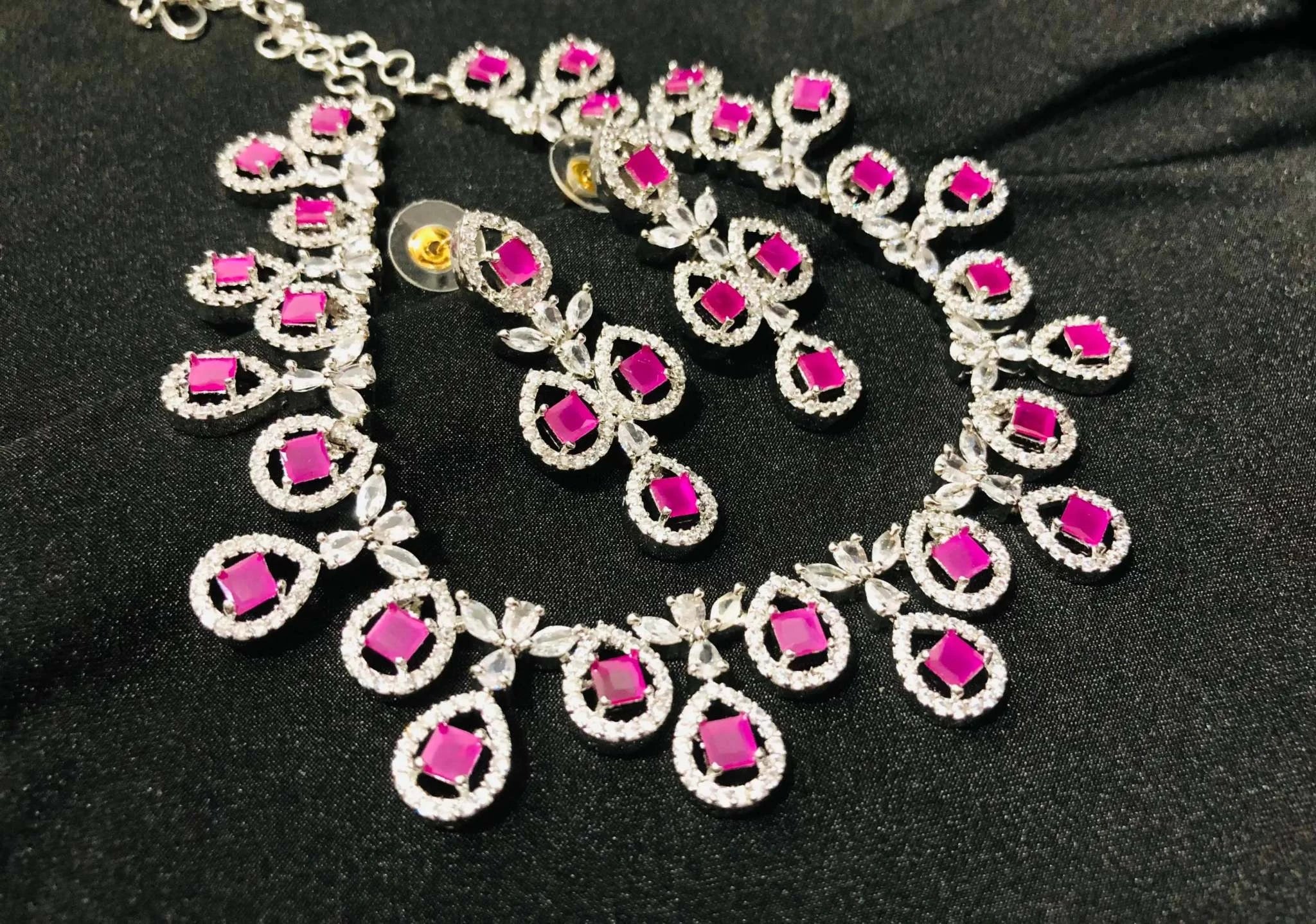 Fuchsia gemstone necklace and earrings set with radiant pink stones and silver detailing on black background