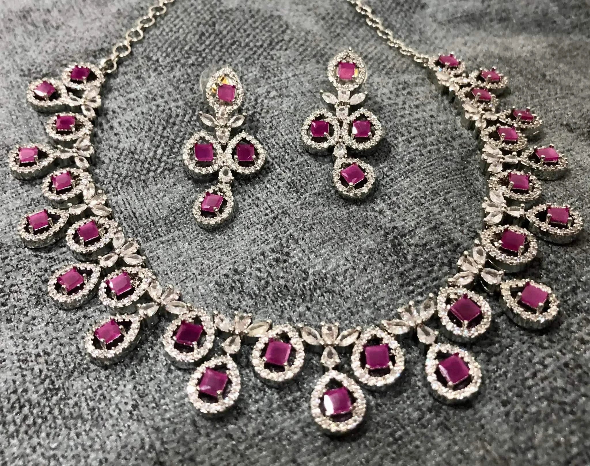 Fuchsia gemstone necklace and earrings set with radiant pink stones and silver detailing on gray background