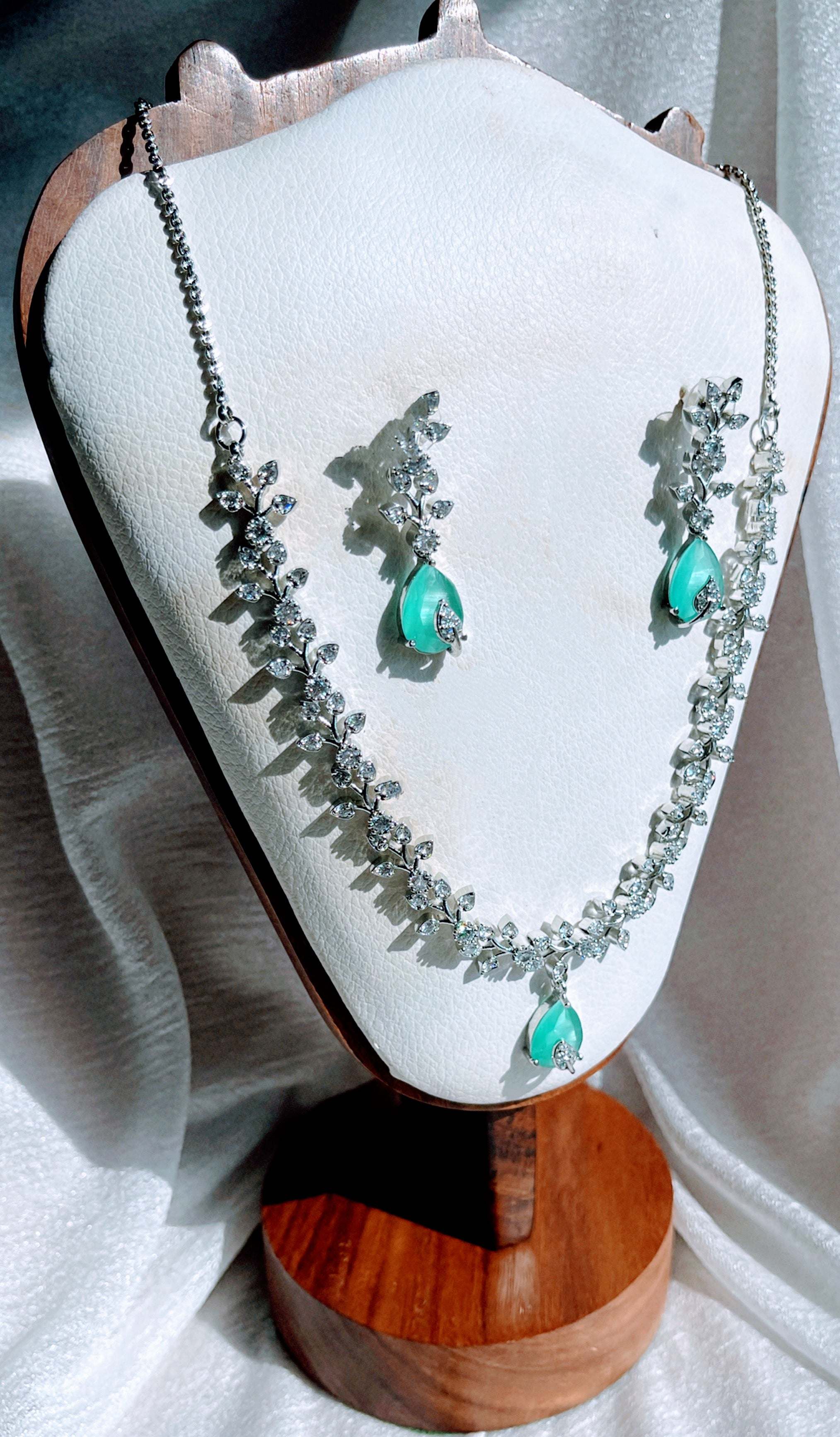 Aqua Boom Amora Necklace Set with silver chain and aqua blue teardrop pendants adorned with sparkling accents displayed on a white jewelry stand