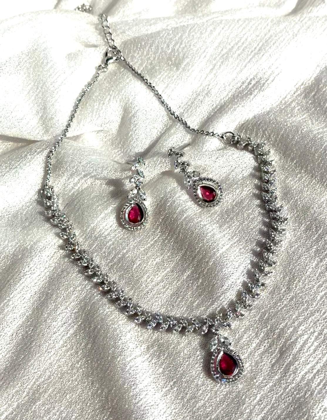 Scarlet Dew Necklace set in silver with bold scarlet teardrop stones and sparkling accents on white fabric background