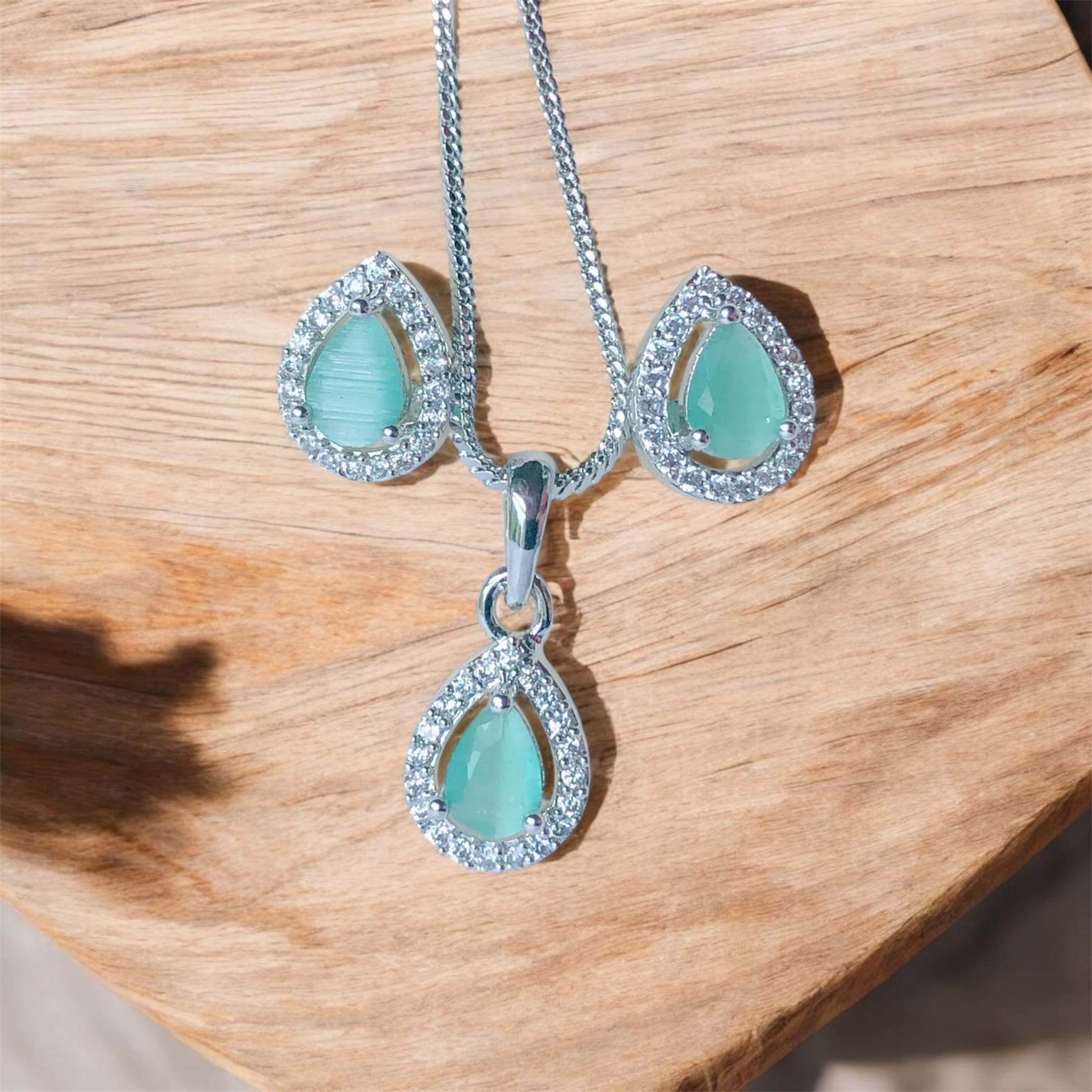 Teal and silver teardrop pendant necklace and earrings set on wooden surface