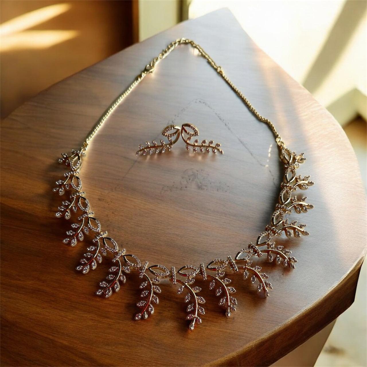 Everglow Willow Necklace Set in gold with delicate leaf design and sparkling accents displayed on wooden surface