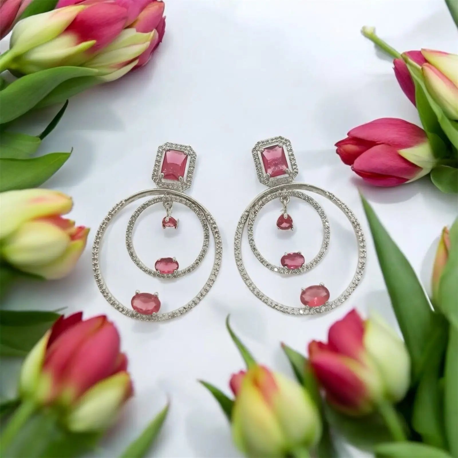 Pink gemstone drop earrings with diamond-studded hoops, framed by vibrant tulips.